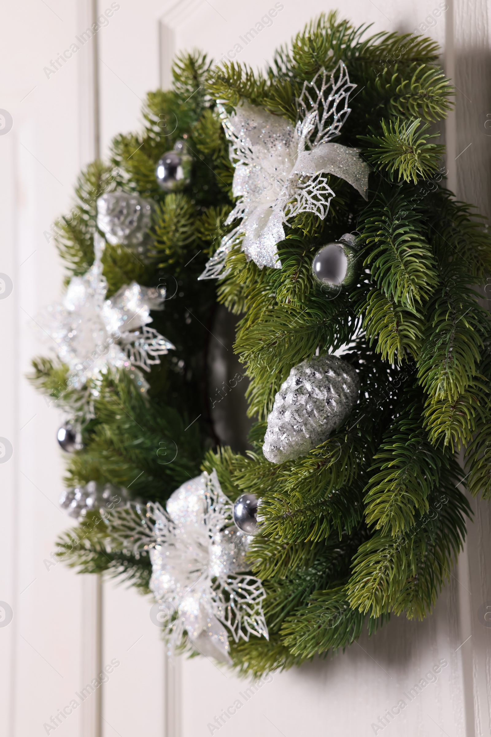 Photo of Beautiful Christmas wreath with festive decor hanging on white door, closeup