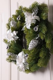 Beautiful Christmas wreath with festive decor hanging on white door, closeup