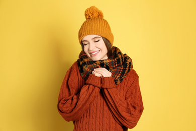 Photo of Young woman wearing warm sweater, scarf and hat on yellow background. Winter season