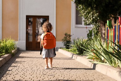 Photo of Little girl walking to kindergarten outdoors on sunny day, back view. Space for text