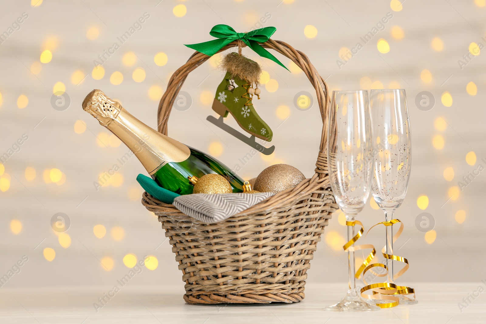 Photo of Bottle of champagne with Christmas balls in wicker basket and glasses on table