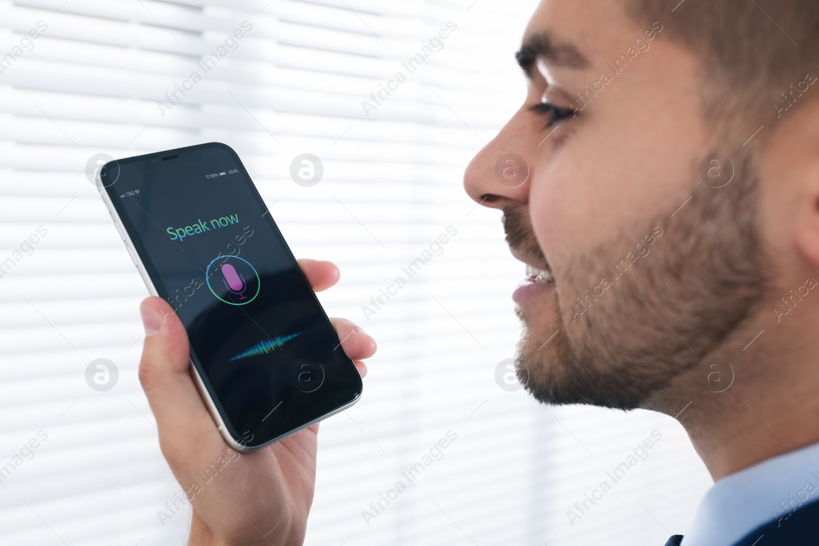 Photo of Young man using voice search on smartphone indoors, closeup