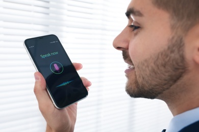 Photo of Young man using voice search on smartphone indoors, closeup