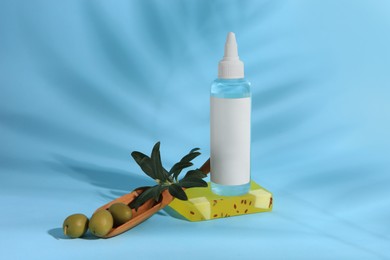 Bottle of cosmetic product, soap bar and olives on light blue background