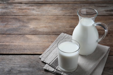 Photo of Jug and glass with fresh milk on wooden table. Space for text