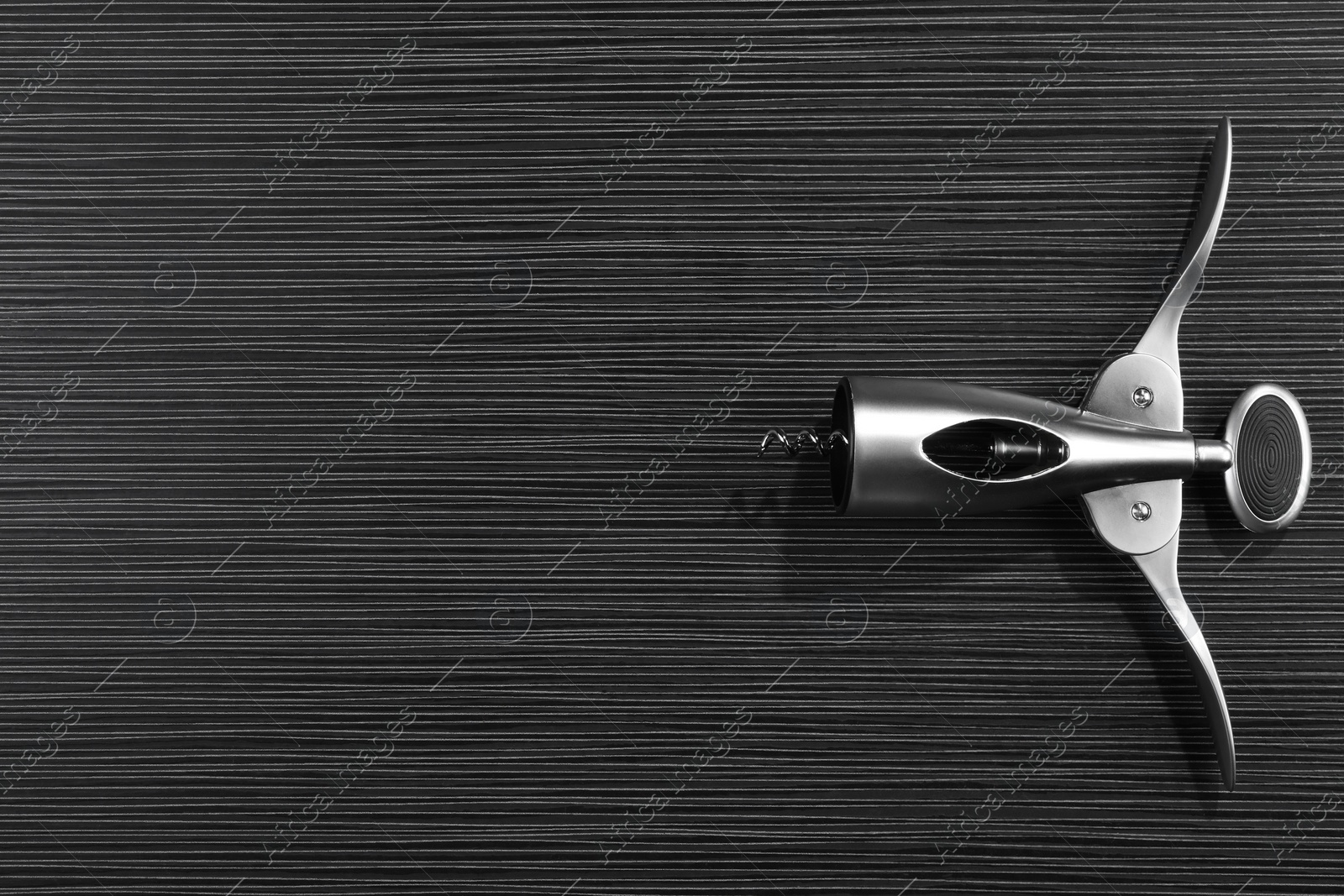 Photo of One wing corkscrew on black wooden table, top view. Space for text