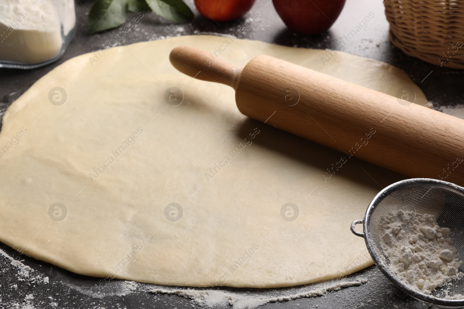 Photo of Fresh dough and rolling pin on grey table, closeup. Making apple pie