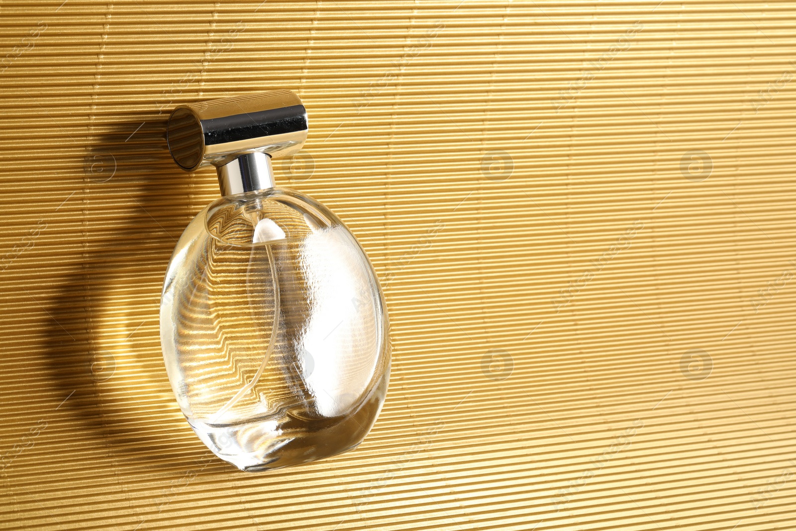 Photo of Luxury women's perfume. Sunlit glass bottle on golden surface, top view. Space for text