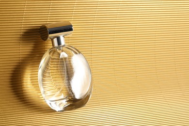 Luxury women's perfume. Sunlit glass bottle on golden surface, top view. Space for text