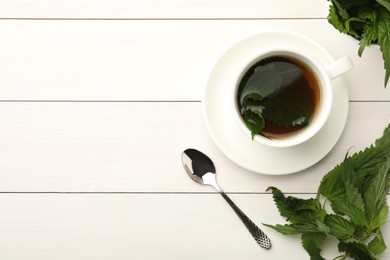 Photo of Cup of aromatic nettle tea and green leaves on white wooden table, flat lay. Space for text