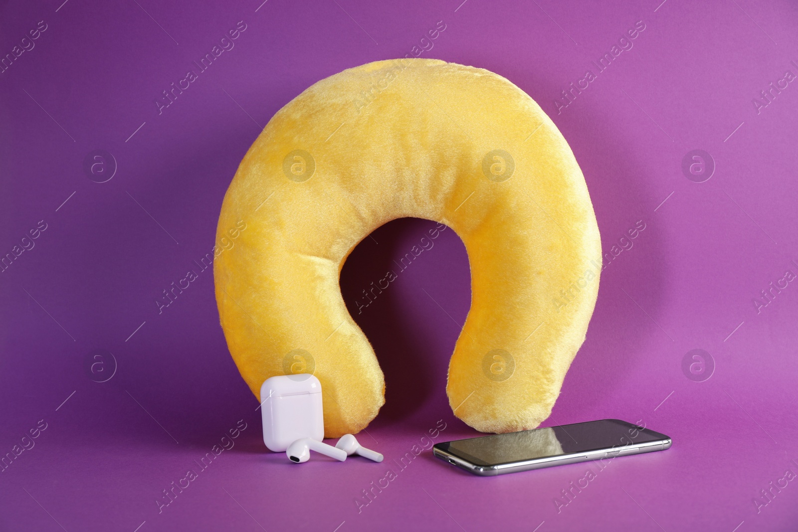 Photo of Yellow travel pillow, smartphone and earphones on violet background