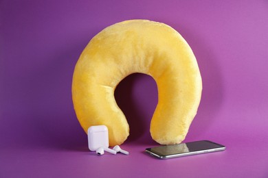 Photo of Yellow travel pillow, smartphone and earphones on violet background