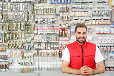 Photo of Salesman standing near showcase with fishing equipment in sports shop. Space for text