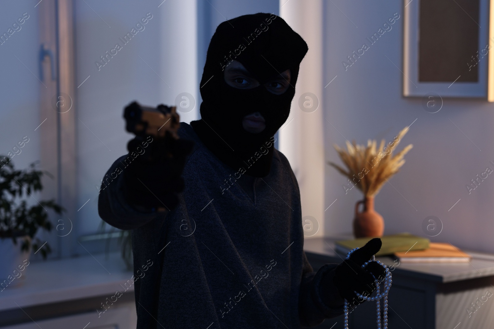 Photo of Thief with gun stealing jewels in foreign house. Burglary