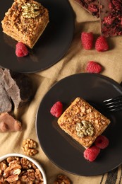 Pieces of delicious layered honey cake with raspberries served on table, flat lay