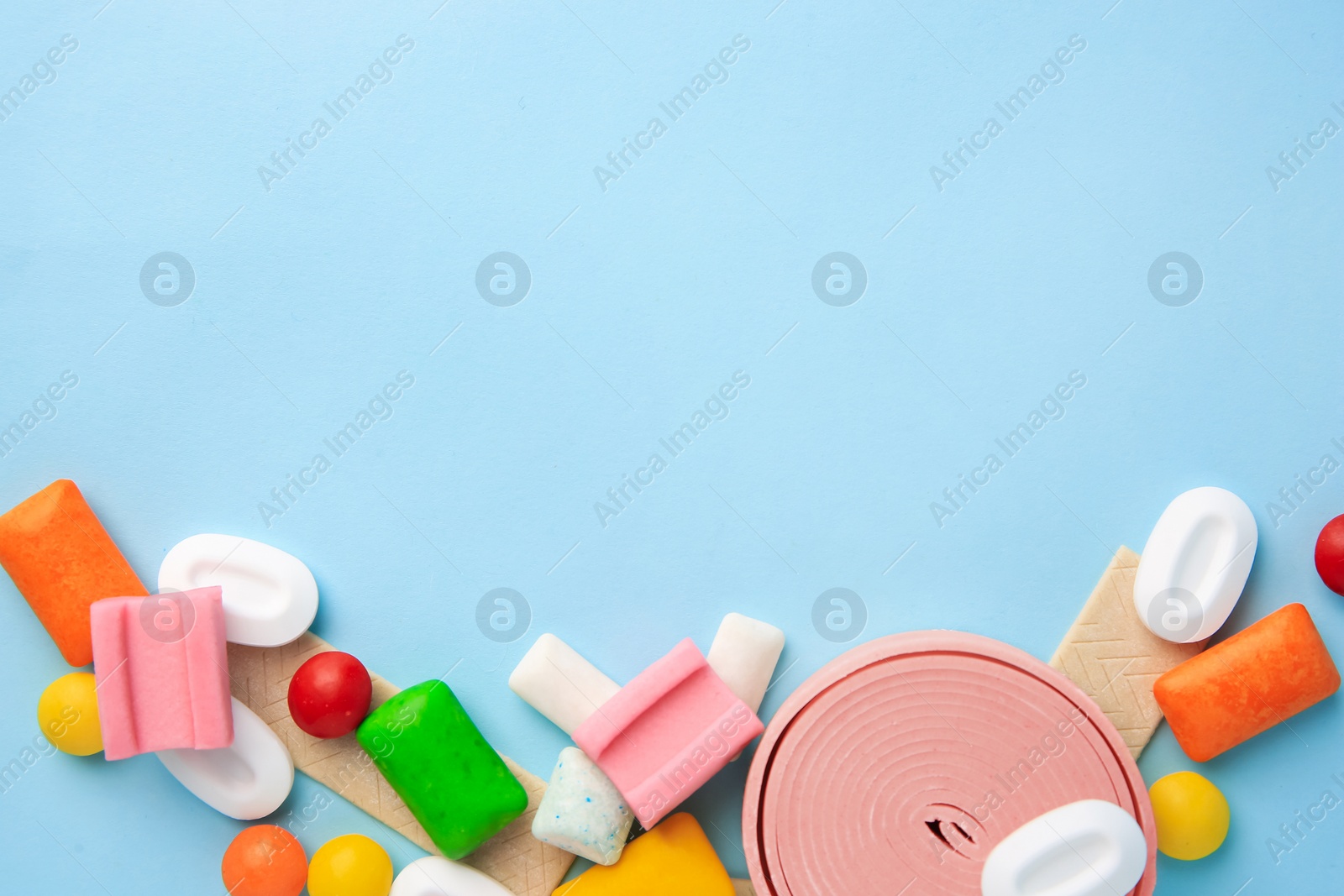 Photo of Many different chewing gums on light blue background, flat lay. Space for text