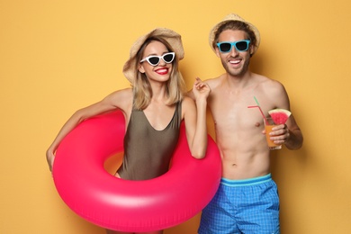 Photo of Happy young couple in beachwear with inflatable ring and cocktail on color background