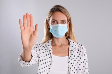 Photo of Woman in protective face mask showing stop gesture on grey background. Prevent spreading of coronavirus