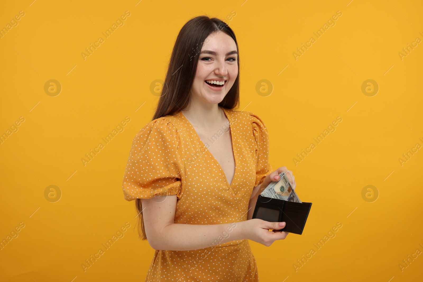 Photo of Happy woman putting money into wallet on orange background