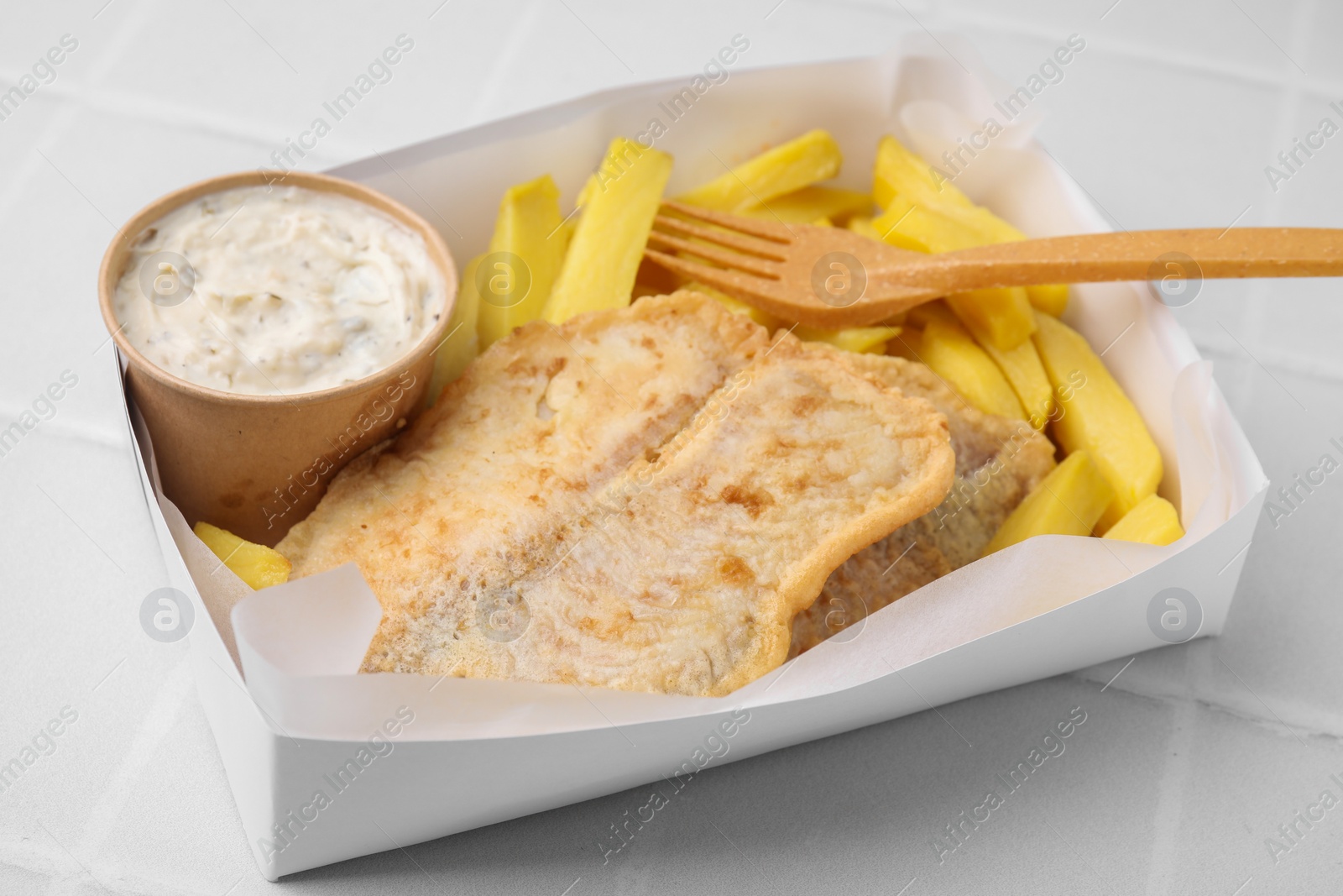 Photo of Delicious fish and chips with tasty sauce served on white tiled table, closeup