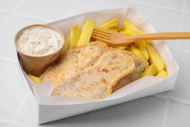 Delicious fish and chips with tasty sauce served on white tiled table, closeup