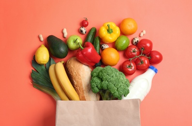 Photo of Paper bag with different groceries on coral background, flat lay