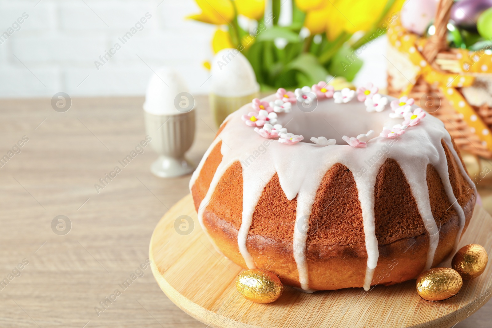 Photo of Delicious Easter cake decorated with sprinkles near eggs on wooden table, closeup. Space for text