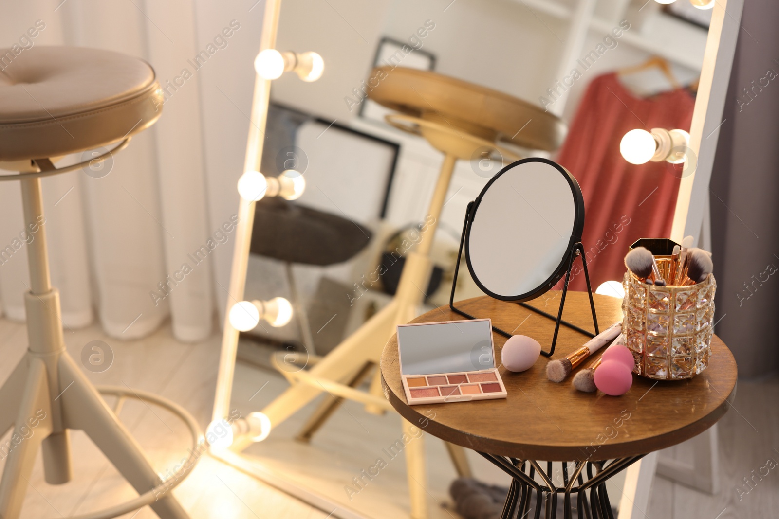 Photo of Makeup room. Stylish mirror with light bulbs and beauty products on wooden table indoors