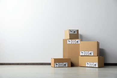 Photo of Many closed cardboard boxes with packaging symbols on floor near white wall, space for text. Delivery service