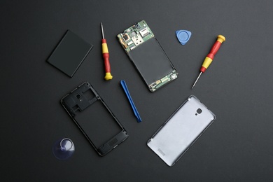 Photo of Disassembled mobile phone and repair tools on black background, flat lay