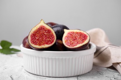 Photo of Bowl of tasty ripe figs on white textured table, closeup