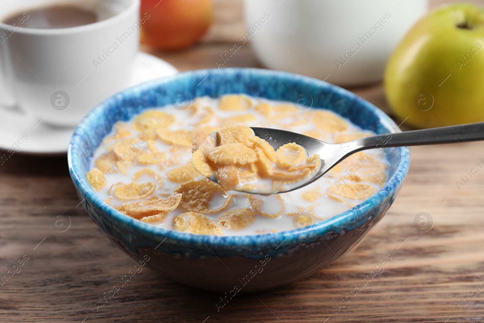 Photo of Healthy cornflakes with milk in bowl served on wooden table, closeup