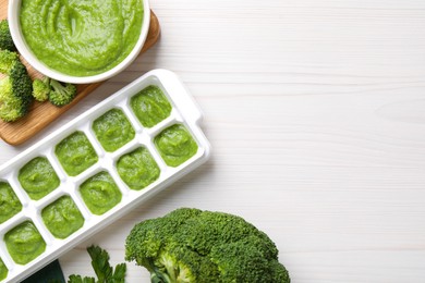 Photo of Broccoli puree in ice cube tray ready for freezing and ingredients on white wooden table, flat lay. Space for text