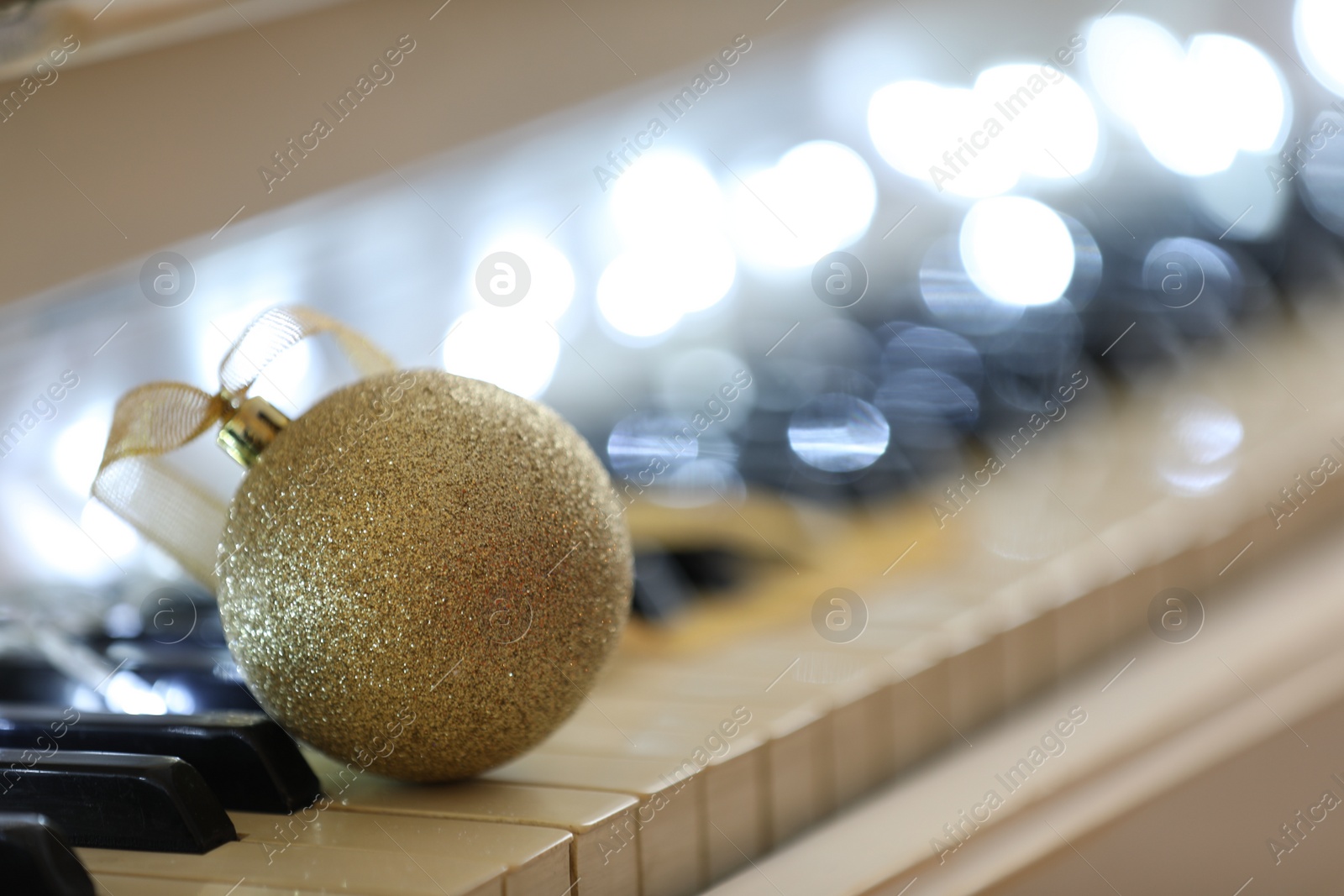 Photo of Beautiful golden bauble and fairy lights on piano keys, space for text. Christmas music