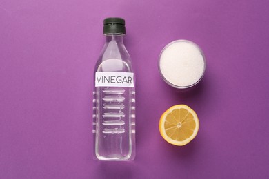 Photo of Eco friendly natural cleaners. Vinegar in bottle, cut lemon and bowl of soda on purple background, flat lay