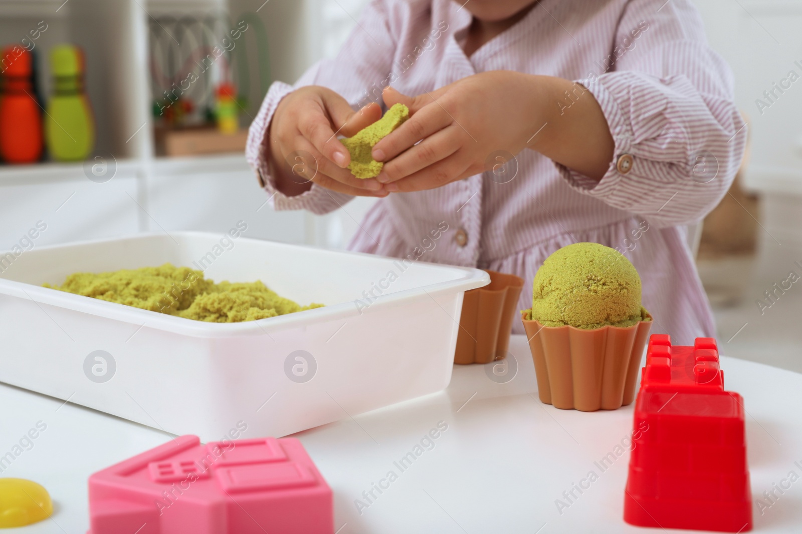 Photo of Little girl playing with bright kinetic sand at table indoors, closeup