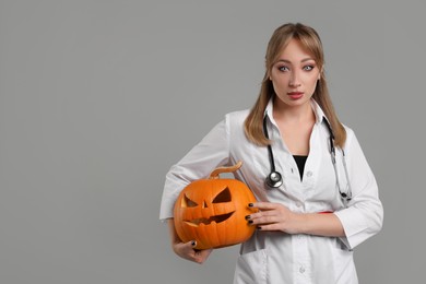 Photo of Woman in scary nurse costume with carved pumpkin on light grey background, space for text. Halloween celebration