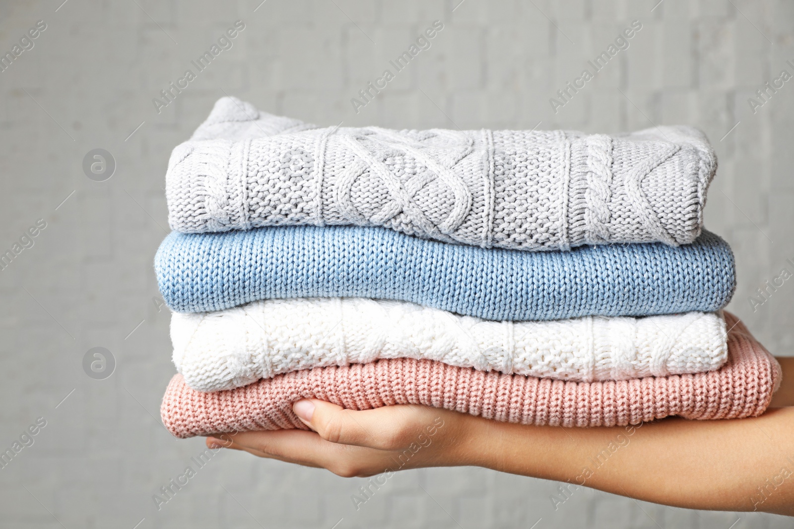 Photo of Woman holding stack of folded warm knitted sweaters against brick wall