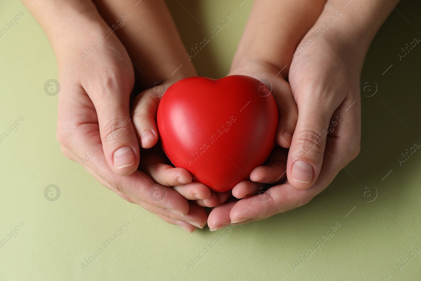 Photo of Mother and her child holding red decorative heart on light green background, top view