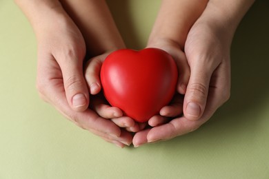 Mother and her child holding red decorative heart on light green background, top view