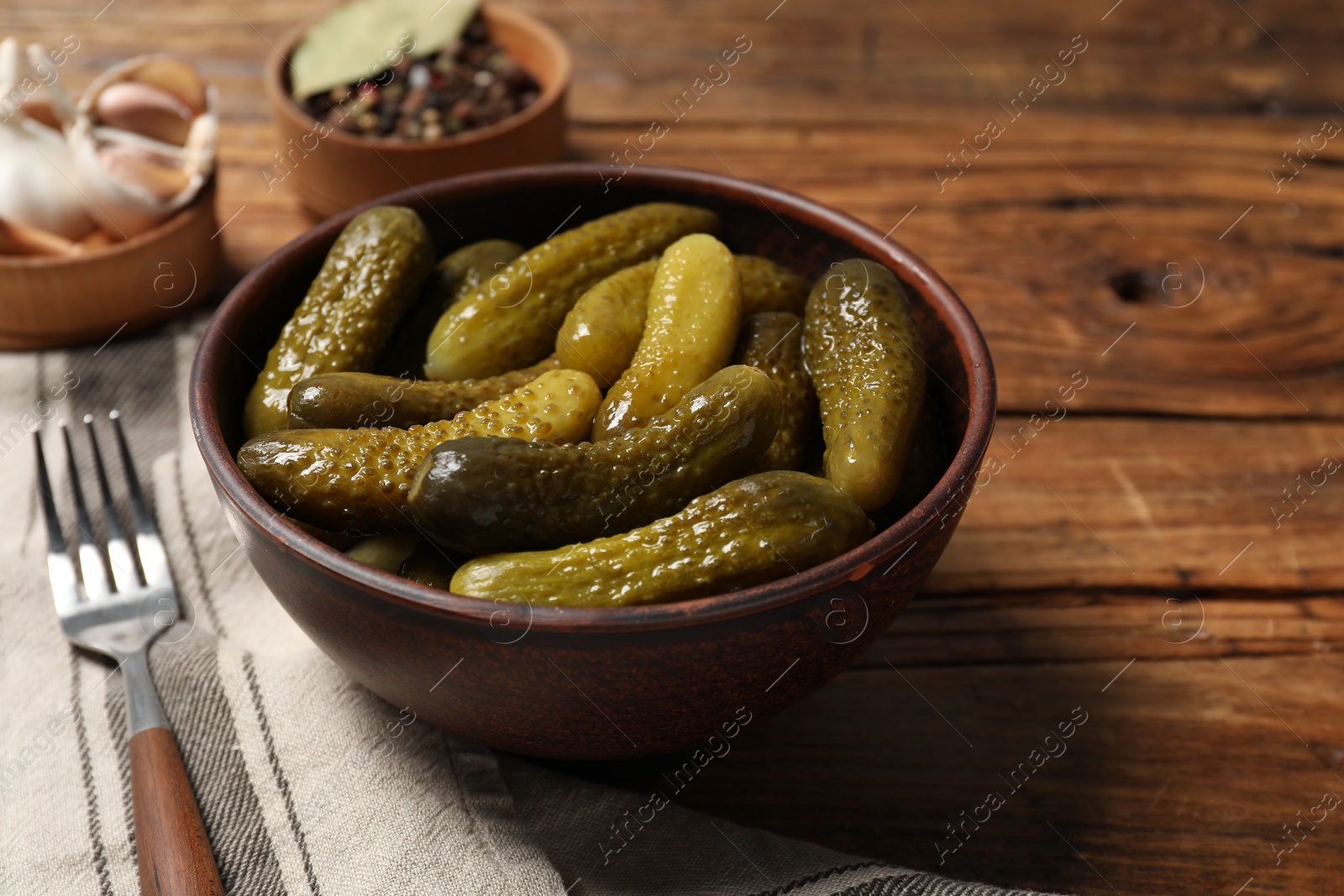 Photo of Tasty pickled cucumbers in bowl and fork on wooden table