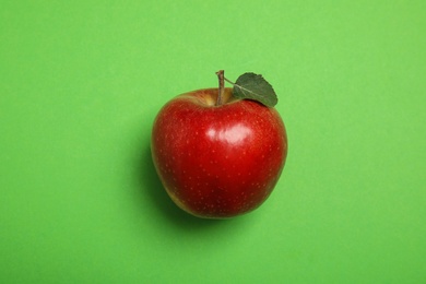 Ripe juicy red apple with leaf on green background, top view