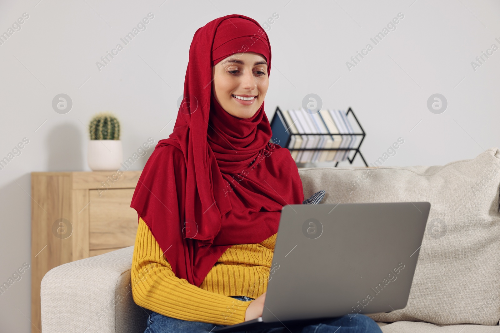 Photo of Muslim woman using laptop at couch in room