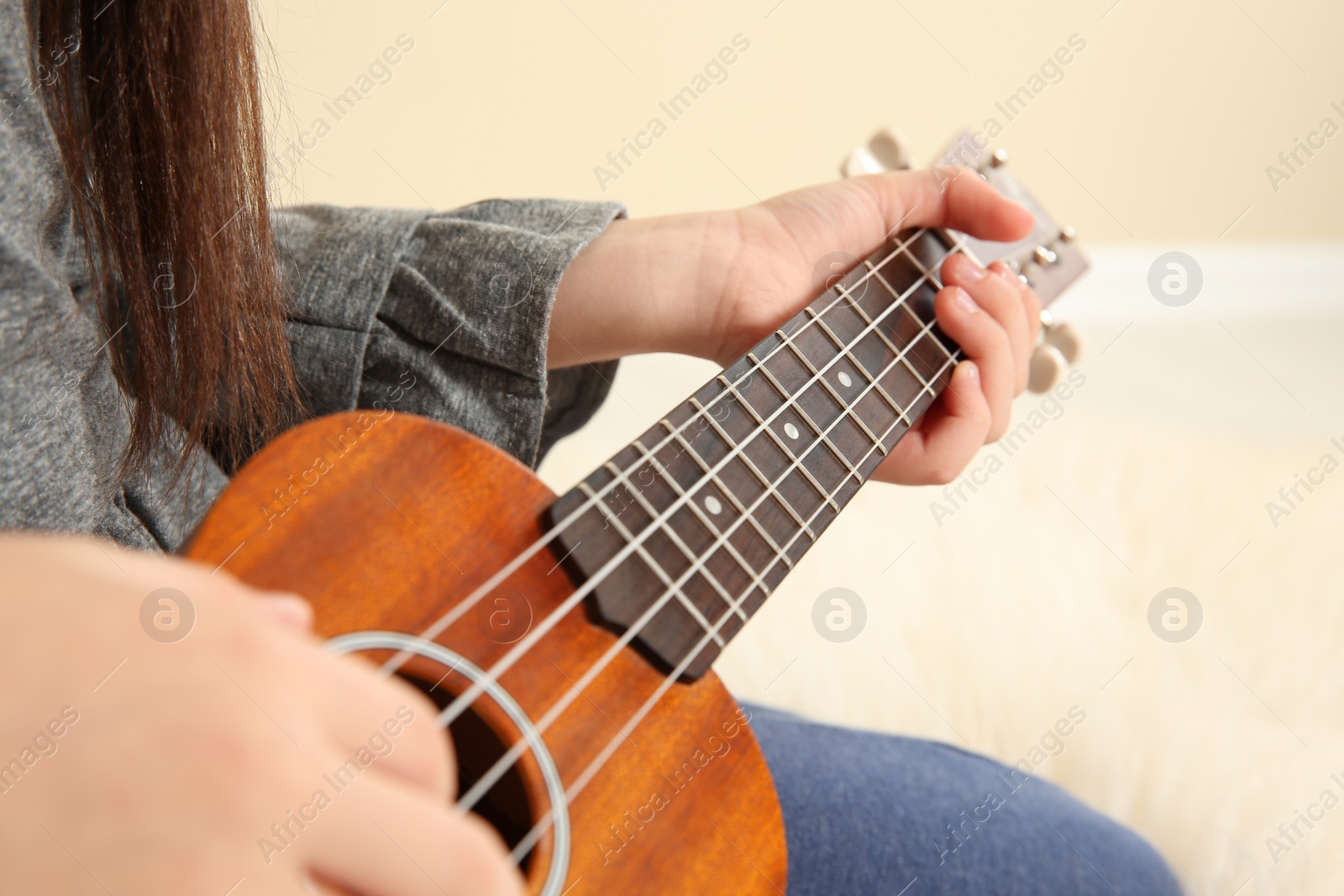 Photo of Little girl playing wooden guitar indoors, closeup