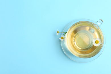 Delicious chamomile tea in glass cup on light blue background, top view. Space for text