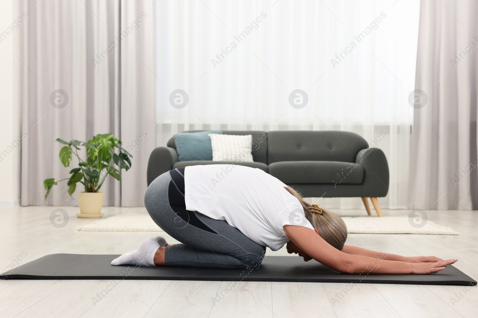 Photo of Senior woman practicing yoga on mat at home