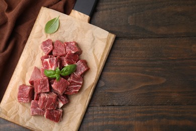 Cut fresh beef meat with basil leaves on wooden table, top view and space for text