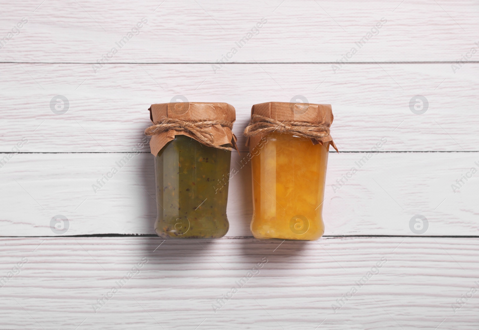 Photo of Jars with preserved fruit jams on white wooden table, flat lay