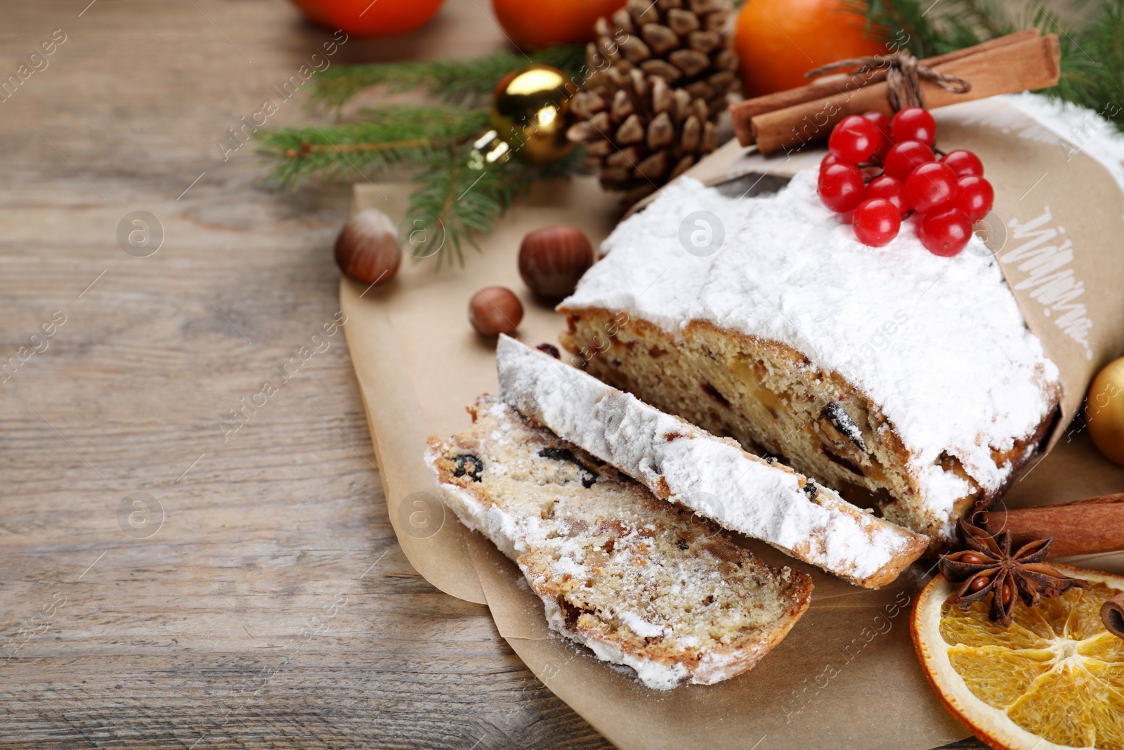 Photo of Traditional Christmas Stollen with icing sugar and cranberries on wooden table, space for text