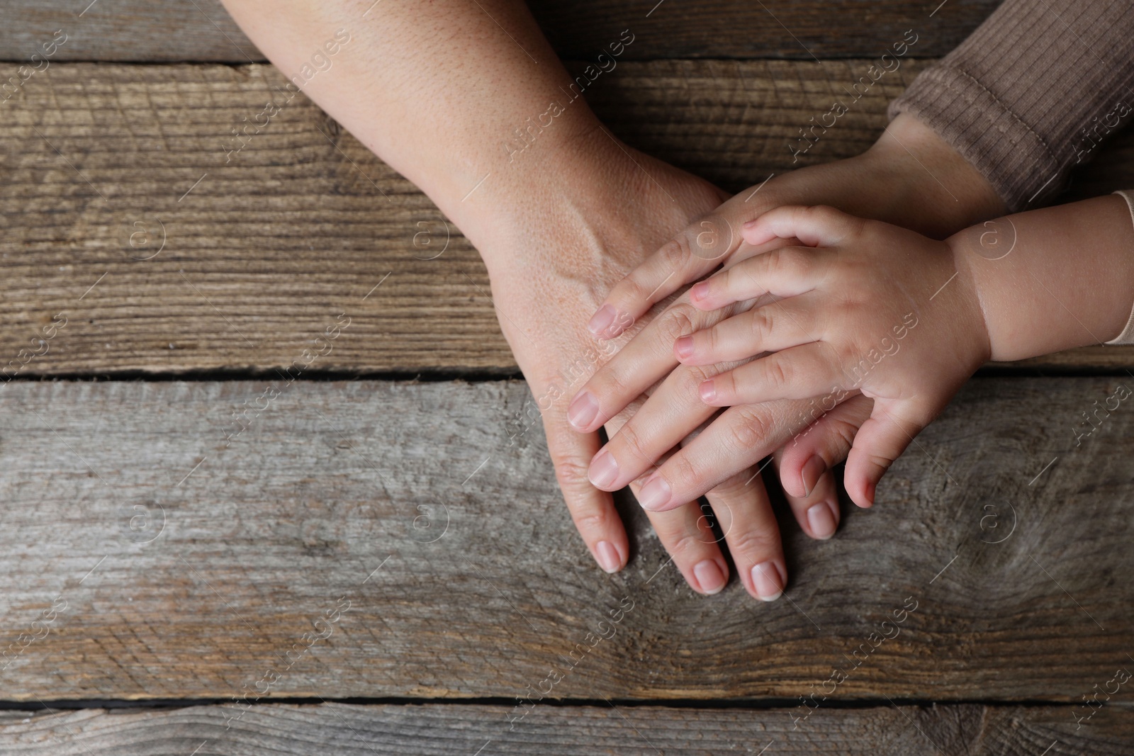 Photo of Family holding hands together at wooden table, top view. Space for text